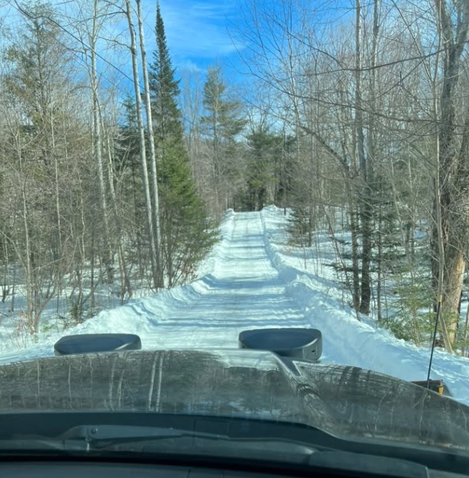 A freshly plowed wooded driveway viewed from a plow truck